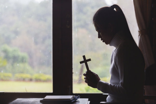 这个女人手持十字架，把经文放在桌子上祈祷。图片下载