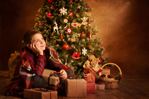圣诞小孩在圣诞树下做梦，快乐男孩带着新年礼物图片下载