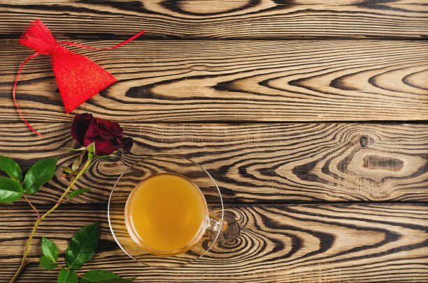 旧木桌上放着绿茶杯，红玫瑰旁放着礼物。前视图。情人节概念图片下载