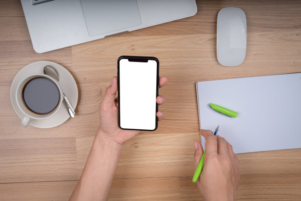 年轻的女商人在办公室打电话。女商人一边用手机发短信一边用笔记本电脑工作。年轻漂亮的女商人坐在工作场所。图片下载