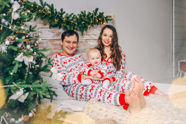 快乐的父母和他们的小女儿穿着节日的衣服，在舒适的房间里有圣诞树、礼物和圣诞灯。图片下载
