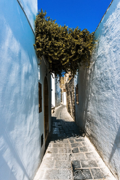 垂直照片与空的街道。街道两边都有白色的房子，这是罗德岛林多斯镇的典型。街道的表面是由方形石头制成的。天空是蓝色的。图片下载