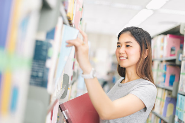 一个亚洲女人从图书馆的书架上挑选一本书。图片下载