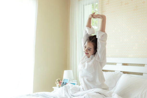 美丽的亚洲女人的笑脸伸展后，醒来享受阳光早上在床上图片下载