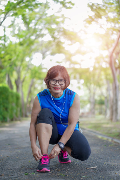 跑步鞋-年长的亚洲妇女慢跑通过公园系鞋带。女性运动健身跑步准备户外慢跑的路上图片下载