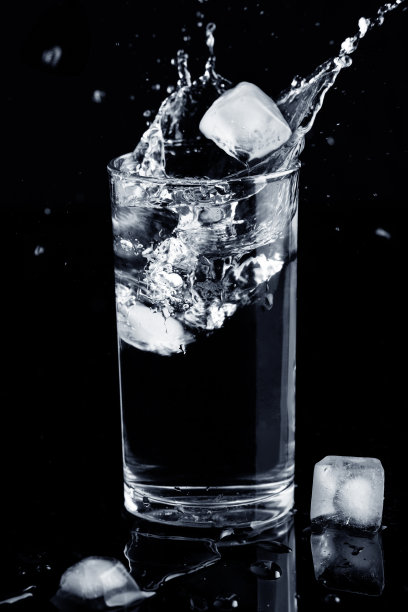 水溅孤立。水溅在带有冰块的玻璃杯中，溢出的水孤立在黑色背景上。健康的概念。图片下载