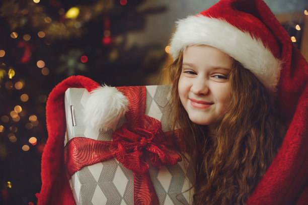 漂亮的小女孩带着礼物，戴着圣诞老人的帽子。圣诞节，新年的概念。图片下载