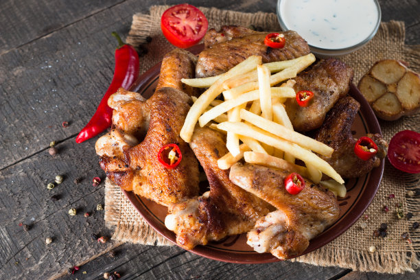 烧烤鸡翅与薯条和啤酒的特写照片。烤肉配酱汁，番茄酱，蛋黄酱。快餐和垃圾食品的概念。图片下载