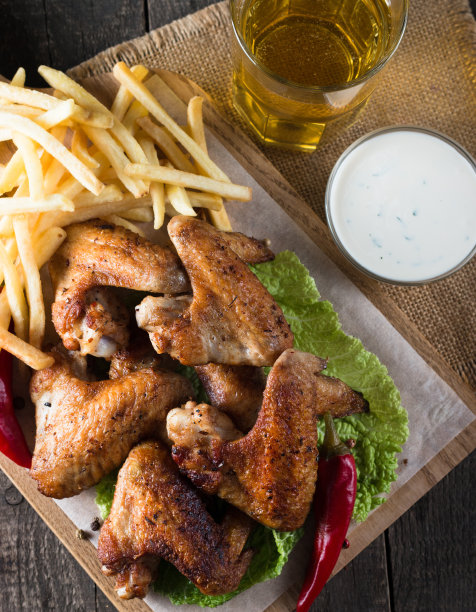 烧烤鸡翅与薯条和啤酒的特写照片。烤肉配酱汁，番茄酱，蛋黄酱。快餐和垃圾食品的概念。图片下载