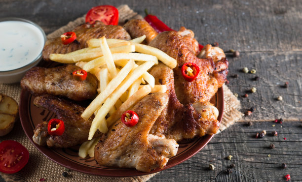 烧烤鸡翅与薯条和啤酒的特写照片。烤肉配酱汁，番茄酱，蛋黄酱。快餐和垃圾食品的概念。图片下载