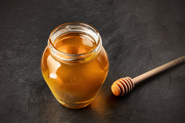 一个蜂蜜勺和罐子的照片在一个黑色的背景和文字的地方。有选择性的重点图片下载