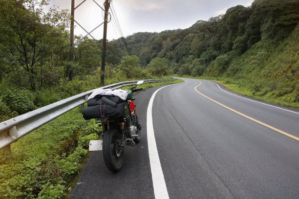 一个骑摩托车的人在通往山顶的路上骑着摩托车。背景是带着行李箱的摩托车旅行者的极端道路图片下载