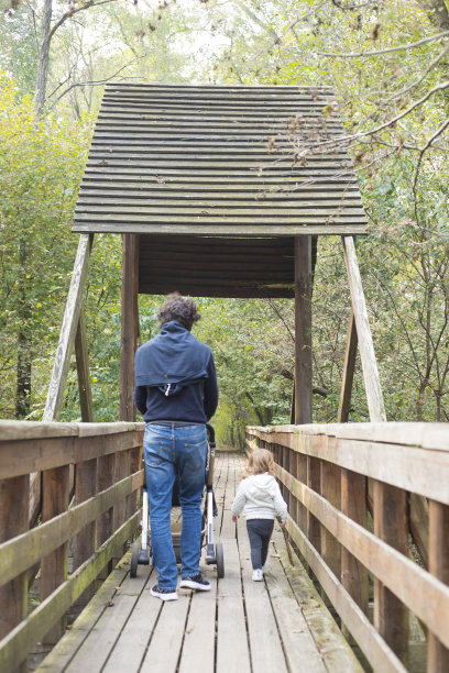 父亲和蹒跚学步的女儿走在一条木制人行道上图片下载