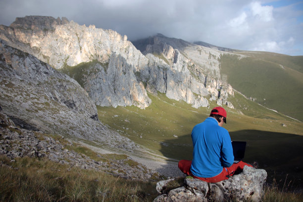 一个人坐在山顶上用笔记本电脑工作。图片下载