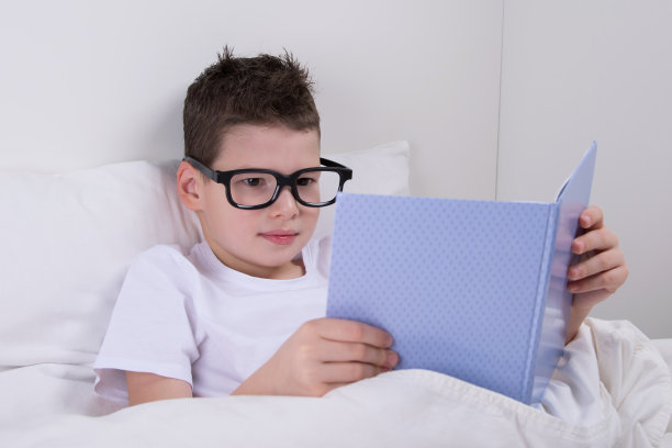 戴眼镜的男孩，躺在床上看书图片下载