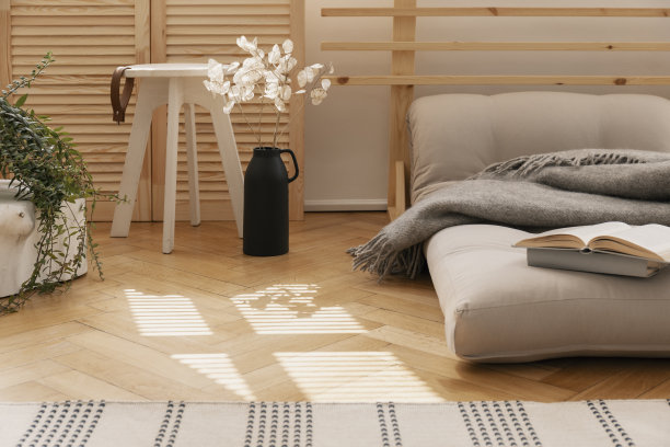 Hygge卧室用斯堪的纳维亚蒲团作为床，旁边是白色的花在黑色花瓶和木制的咖啡桌，真实的照片图片下载