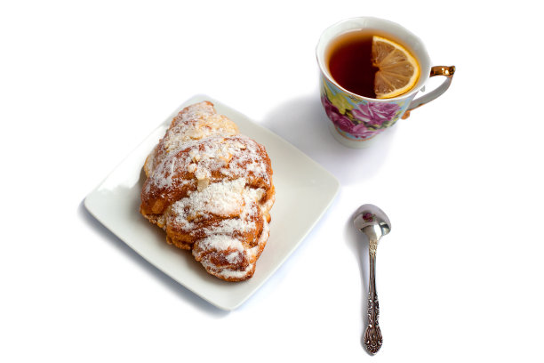 白盘子上放着牛角面包，配上一杯柠檬茶和一个甜点勺，背景是白色的图片下载