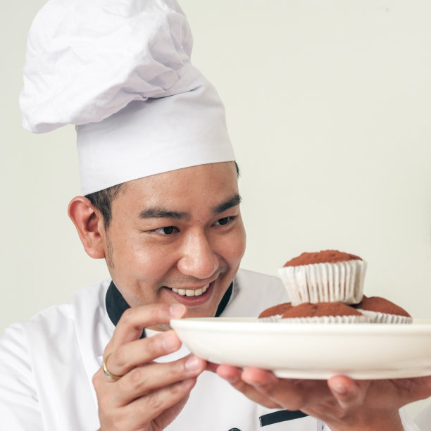 糕点师拿着白色盘子上的纸杯蛋糕，在上桌前检查。图片下载