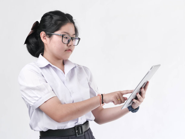 穿着制服的亚洲学生在白色背景上使用平板电脑。图片下载