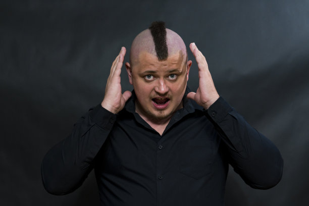 穿着黑色衬衫，留着莫霍克发型的朋克。手指举到头上。愤怒和惊讶的表情。图片下载