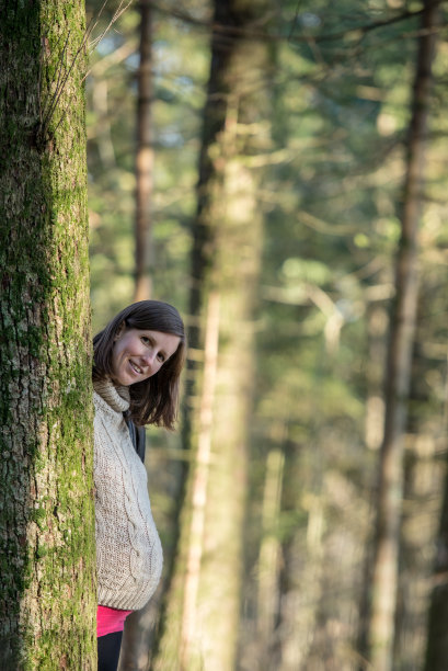 一个年轻孕妇站在森林的一棵树后面图片下载