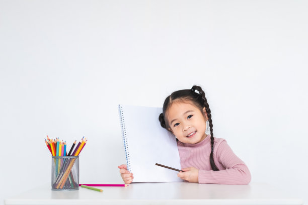 亚洲女孩在白色的背景上用许多彩色铅笔在白纸上画画图片下载