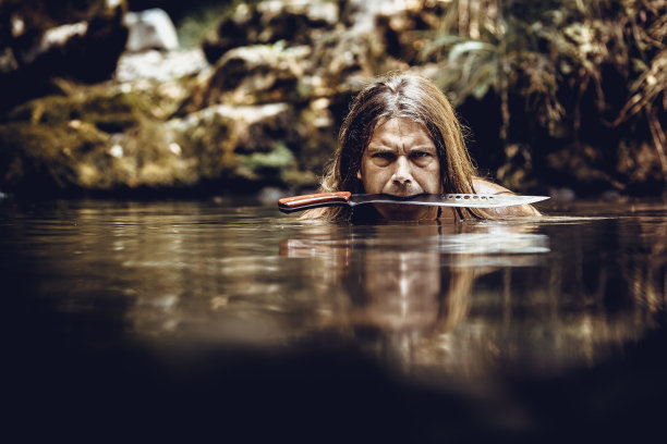 一个嘴里叼着弯刀在小溪里游泳的成年人图片下载
