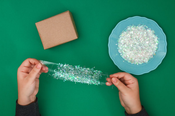 最初设计的圣诞礼物由牛皮纸、透明胶带和切割发光塑料，玻璃纸上的绿色背景。一步一步在照片上。手工DIY。图片下载