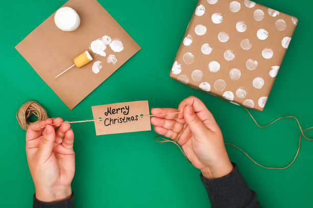原设计的一份圣诞礼物的牛皮纸，白色的油漆，一枚土豆邮票。一步一步在照片上。手工制作的,DIY。一份用棕色纸包着的礼物，上面还有白色的圆点。图片下载