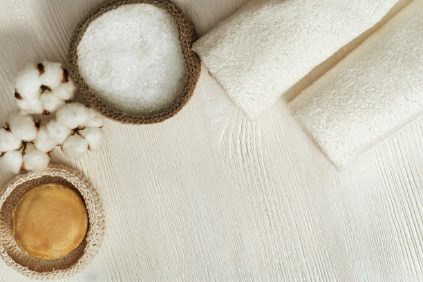 水疗中心的背景。棉花植物的蓬松的花，海盐，干净的卷毛巾，圆形的肥皂在白色的木制背景与复制空间。水疗中心的概念。健美的照片。图片下载