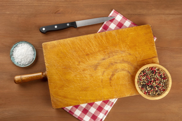 这是一张切菜板的照片，从上面拍摄在一个黑色的乡村纹理上，用盐，胡椒，刀，格子布，和一个地方的文字。一个烹饪背景与复制空间图片下载