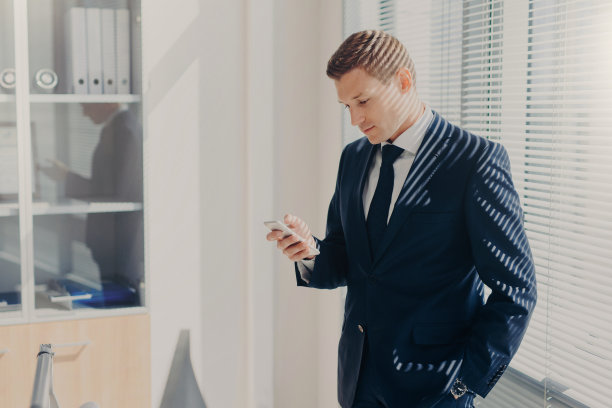 办公室员工的照片，穿着优雅的服装，有吸引力的外表，使用现代手机，查看通知，摆姿势在宽敞的柜子，连接无线网络。网络的概念图片下载