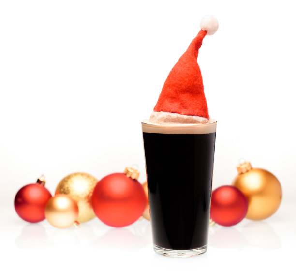 黑麦啤酒品脱玻璃杯与圣诞红帽和圣诞小玩意在背景上的白色图片下载