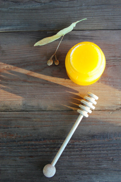 蜂蜜罐与木制蜂蜜勺和酸橙树种子在乡村棕色木制背景。有选择性的重点。图片下载