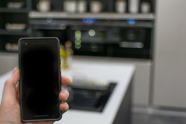手用智能手机作为智能家居控制应用，对模糊的厨房背景，智能家居的概念图片下载