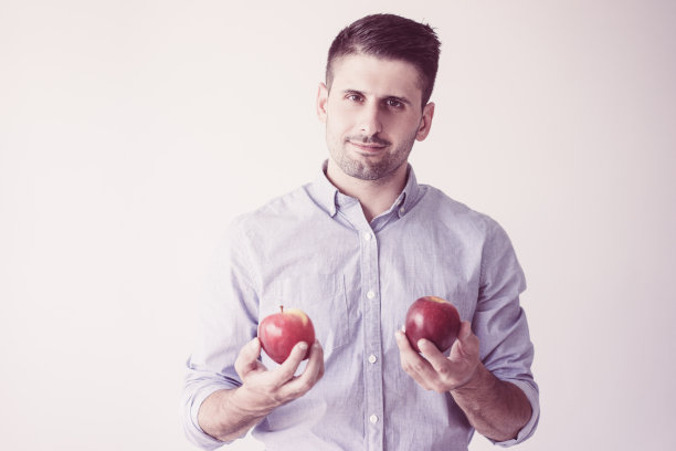 微笑的年轻白人男子举着两个红苹果的肖像图片下载
