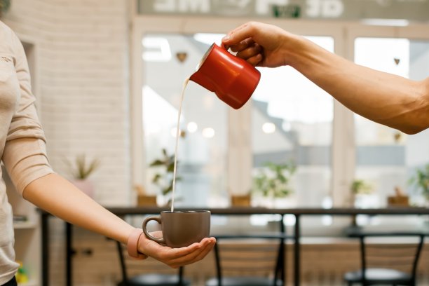 特写倒蒸牛奶到咖啡杯，咖啡店背景图片下载