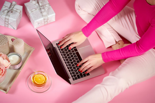 女性手放在笔记本电脑键盘上的俯视图，粉色背景上的蜡烛、鲜花和礼物图片下载
