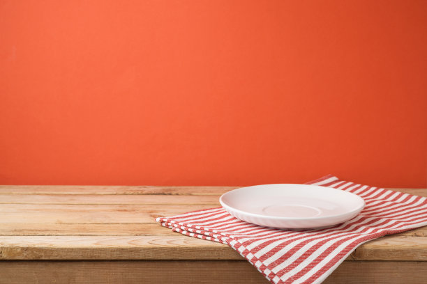 红色墙壁背景的木桌上空着白色盘子和桌布图片下载