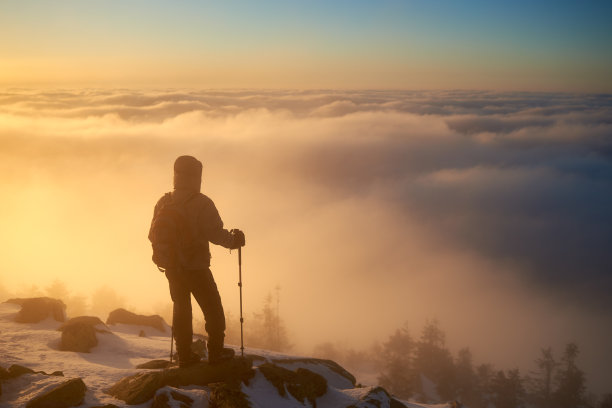 游客背包在岩石山的背景雾蒙蒙的山谷和日出时的蓝天。图片下载