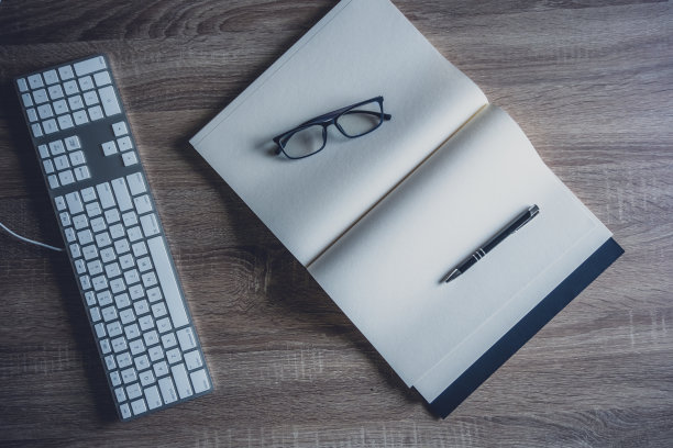 办公桌边，商务用键盘，黑色笔记本，钢笔，眼镜。俯视图背景的复制空间。黑色的桌子上。图片下载
