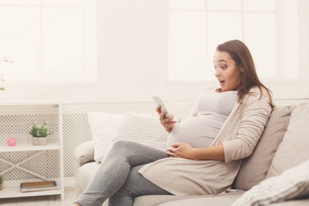 惊讶孕妇在家里使用智能手机图片下载