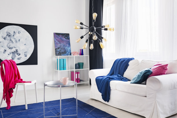在客厅里，白色沙发上铺着蓝色的毯子，椅子上铺着粉红色的布，上面贴着海报。真实的照片图片下载
