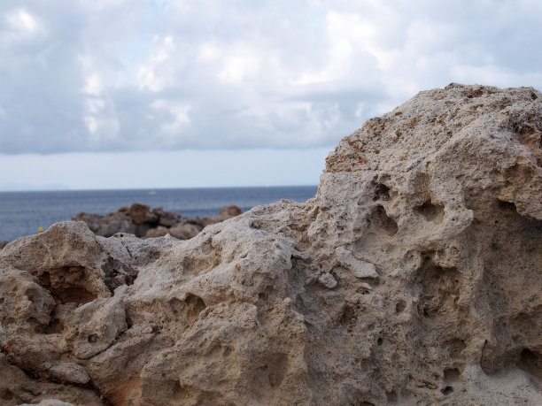 崎岖的岩石对深蓝色的海洋与明亮的天空与白色的云在西班牙梅诺卡旅行或度假背景图片下载