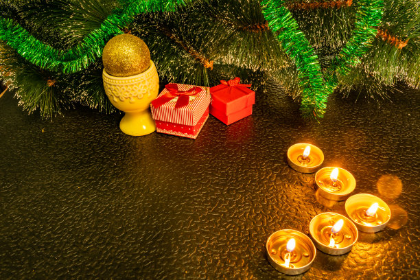 用蜡烛、礼品盒和银珠子组成的圣诞礼物。除夕的装饰品。在温暖的灯光装饰的黑暗背景下，松柏之间的圆锥体和灯光与碑文的空间图片下载