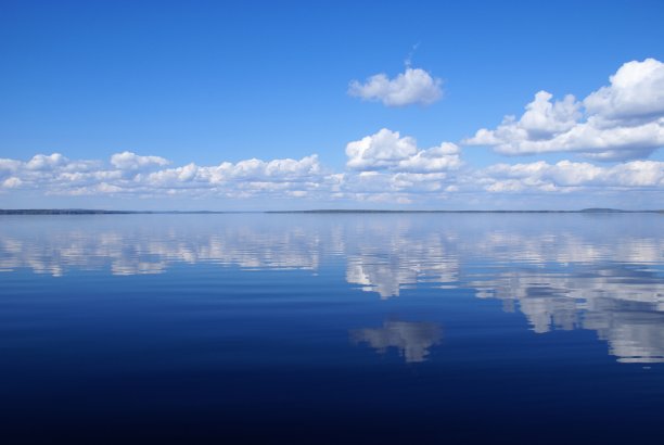 美丽平静的蓝色湖泊与白云在水中的反射。天气晴朗，阳光灿烂。天空是蓝色的。地平线上的岛屿。图片下载