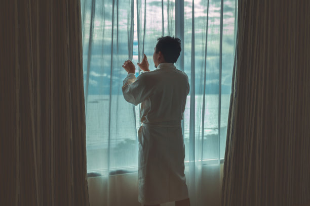 早上在豪华酒店的床上醒来，穿着浴袍的亚洲男子打开并观赏海滩，生活方式和度假理念图片下载