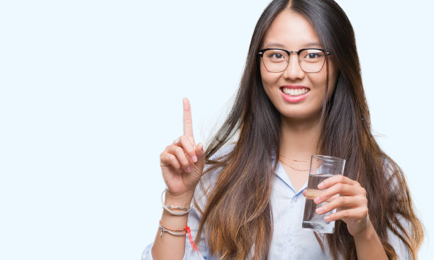 一名年轻的亚洲女性在孤立的背景下喝一杯水，对一个想法或问题感到惊讶，并开心地指着对方，第一图片下载