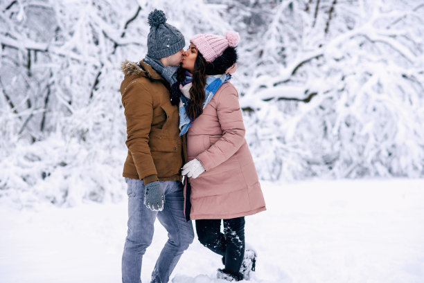 一个美丽的孕妇和她的丈夫在一个下雪的冬天的公园温柔的吻图片下载