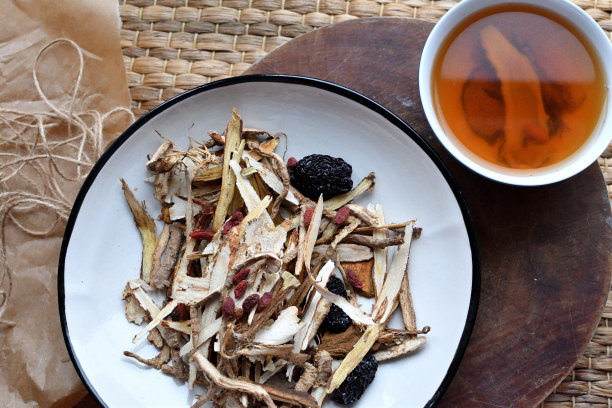 中药。用红枣、枸杞、人参等草药茶放在白色的盘子里，在中性的背景上。侧视图和俯视图。图片下载